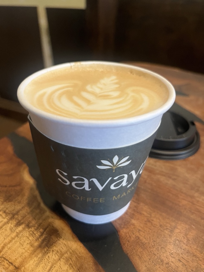 A Savaya to-go cup with rosetta latte art on a wood table.